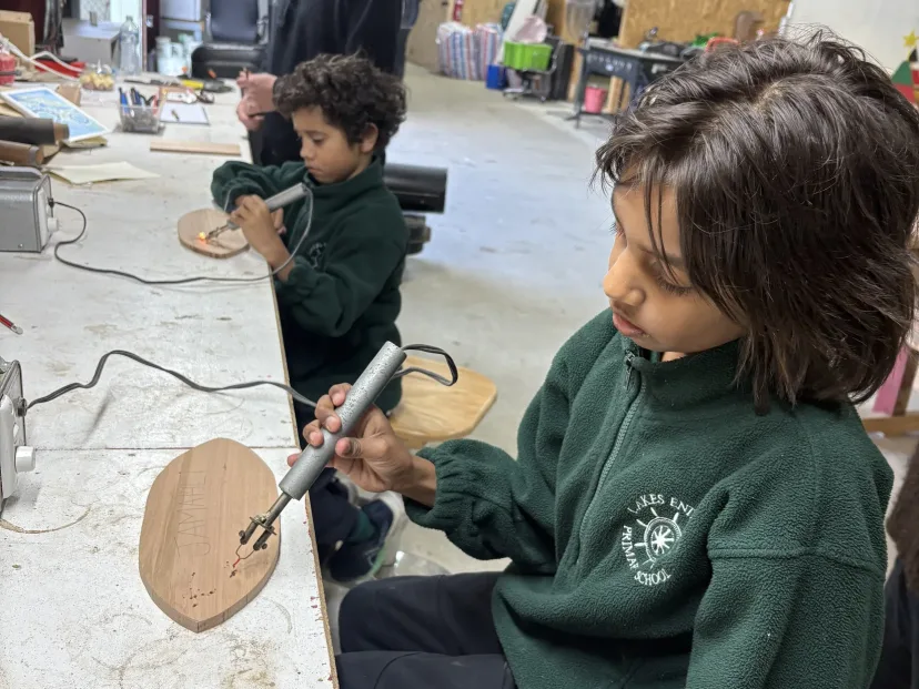 A student shaping a timber board with a rotary tool