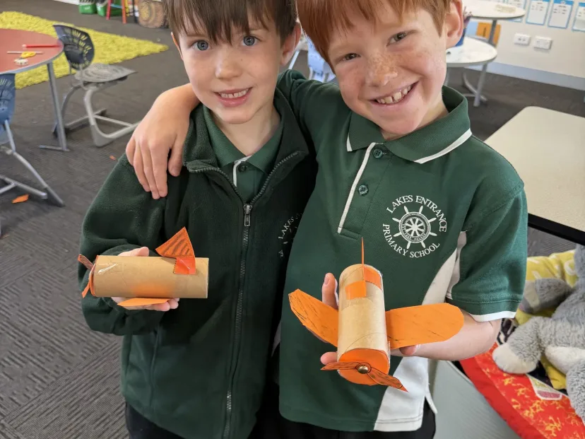 Two students with their arms round each other holding model planes they built
