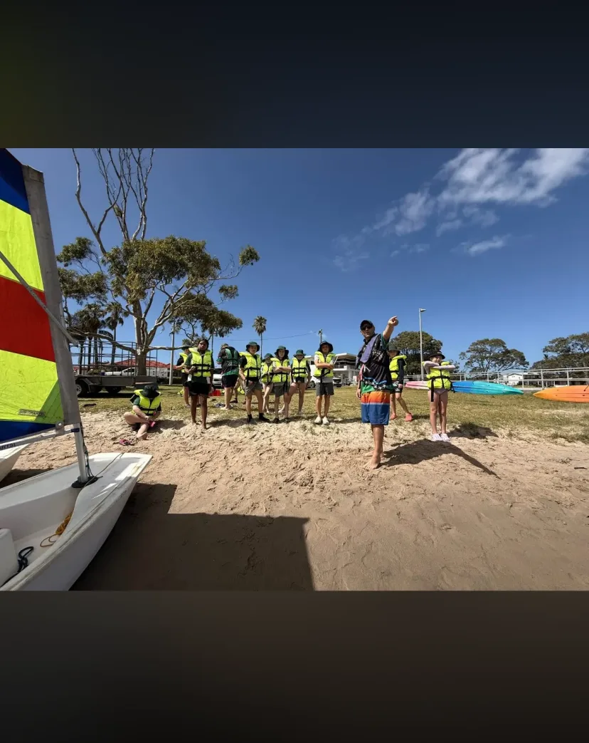 Students in life jackets on the sand beside the sailing dinghies
